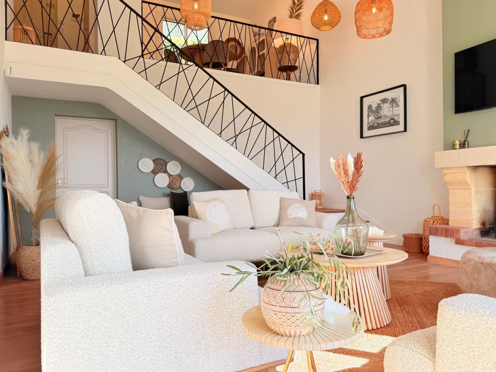 Salon lumineux de la Villa Plen Souleù à Cabris, avec canapé bouclé, cheminée et escalier vers mezzanine.